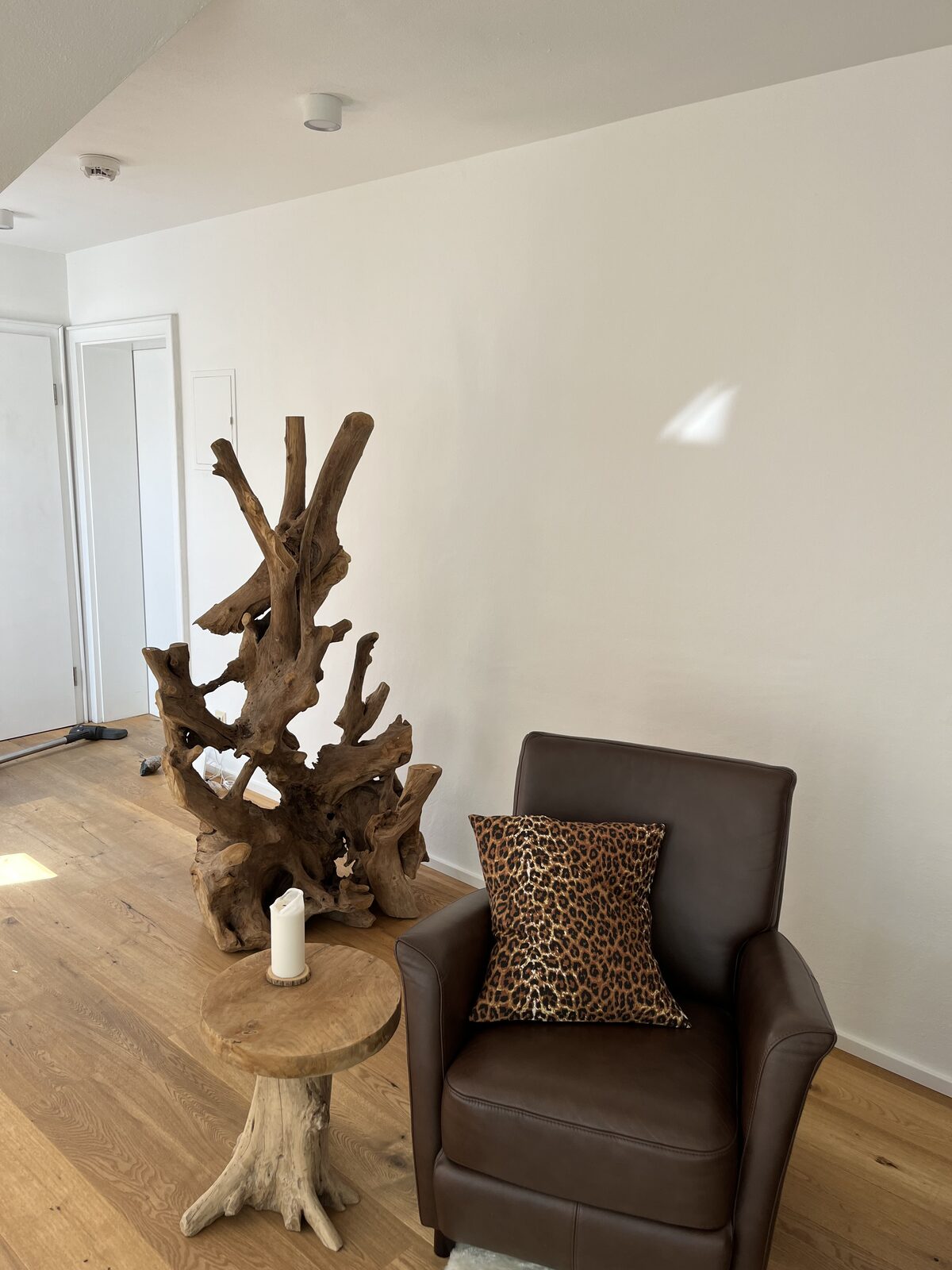 Brauner Ledersessel vor einer hellen Wand, daneben eine Wurzelholzskulptur und ein Beistelltisch aus Holz