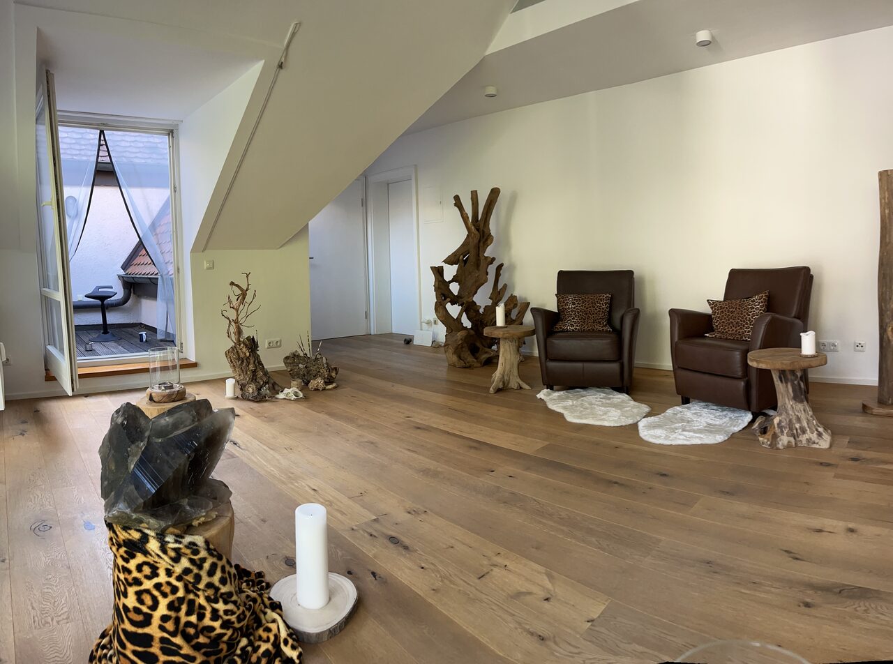 Sitzbereich mit zwei Ledersesseln und Beistelltischen aus Holz, daneben eine geöffnete Balkontür